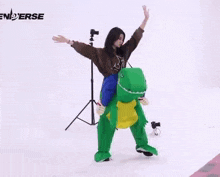 a person in a green dinosaur costume is doing a handstand on a white surface .