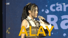 a woman singing into a microphone with the word alay in yellow letters