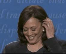 a woman is smiling and touching her hair while wearing pearls