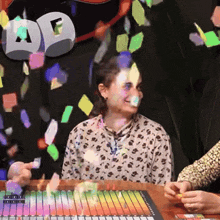 a woman sitting at a table with confetti falling around her and a sign that says ' ae ' on it