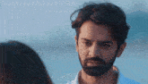 a man with a beard and a white shirt is looking at a woman on the beach .