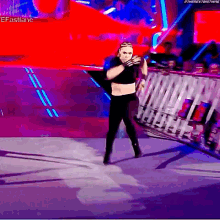 a woman in a black crop top and black pants is standing on a stage in front of a crowd .