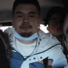 a man with a beard wearing a mask and a necklace is sitting in a car .