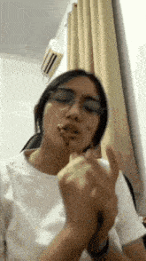 a woman wearing glasses and a white shirt is eating a sandwich .