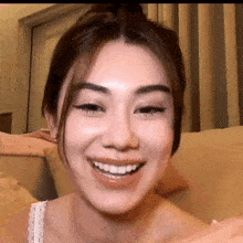 a woman is smiling while sitting on a couch and looking at the camera .