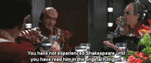 two men are sitting at a table drinking wine and one of them is talking about shakespeare .