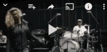 a woman singing into a microphone while a drummer plays drums