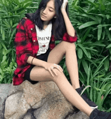 a girl is sitting on a rock with her legs crossed and a shirt that says feminist on it