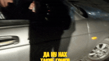 a man is standing in front of a silver car with the words da hy hax written in yellow