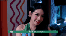 a woman in a green dress is smiling in front of a colorful wall with the words honeycam.org at the bottom