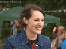 a woman in a denim jacket smiles in front of a green tent with the hashtag @itsscottiesstark