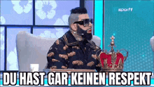 a man with a beard and sunglasses is sitting in a chair wearing a crown and a microphone .