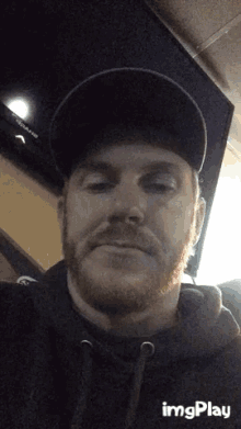 a man with a beard is wearing a hat and a black hoodie while looking at the camera ..