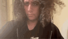a man with long curly hair is making a funny face while looking at the camera .