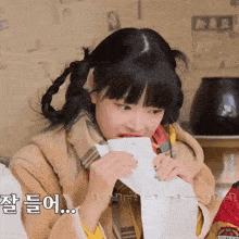 a girl wearing a plaid scarf is holding a piece of paper in front of her mouth with korean writing on it