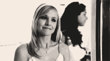 a woman is smiling in front of a mirror while another woman is standing behind her .
