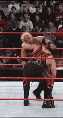 two men are wrestling in a wrestling ring with a crowd watching .