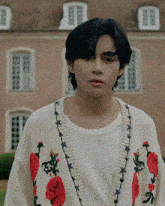 a young man wearing a white shirt and a white cardigan with red roses on it