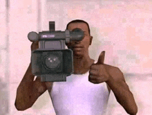 a man in a white shirt is holding a video camera and giving a thumbs up .