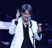 a man in a white jacket holds a bell in front of a microphone