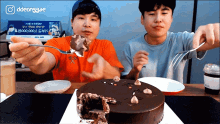 two men are eating a chocolate cake with a sign that says ddeongae in the background