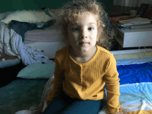 a little girl wearing a yellow shirt is sitting on a bed