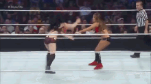 two women are wrestling in a wrestling ring with a referee watching .