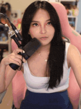 a woman in a white tank top is holding a microphone in front of her face .