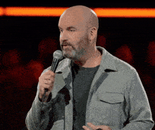 a bald man with a beard is holding a microphone in his hand