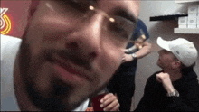 a man wearing glasses and a white hat looks at the camera while another man looks on