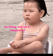 a little girl is sitting in a white chair with the words aiu không nho em a baoyenn ne written in pink