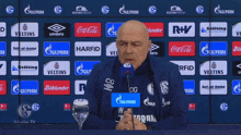 a man speaking into a microphone in front of a wall of advertisements including coca cola