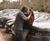 a man and a woman are kissing in front of a parking lot full of cars .