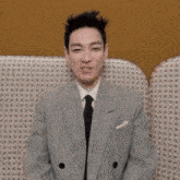 a man in a suit and tie is sitting on a couch with his hands in the air .