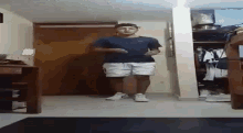 a man in a blue shirt and white shorts is standing in a room in front of a closet .