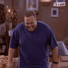 a man in a blue shirt is dancing in a living room with a tv land logo on the wall behind him