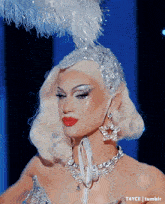 a close up of a drag queen wearing a feathered headpiece and a necklace