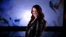 a woman wearing a black leather jacket is smiling in front of a blue background