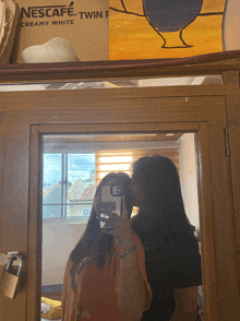 two girls are kissing in front of a nescafe box