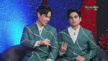 two men in green suits are sitting next to each other in front of a screen that says " kapamilya " on it