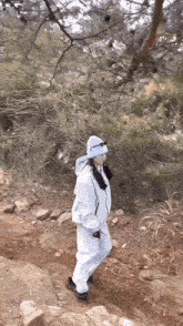 a woman in a white jumpsuit is walking on a rocky path