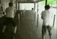 two men are walking down a hallway and one of them is jumping over a railing .