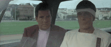 two men are sitting in a car and one has a headband around his head