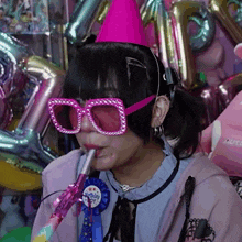 a girl wearing pink glasses and a pink party hat is blowing a party horn