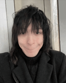 a person with long black hair and a black coat making a funny face