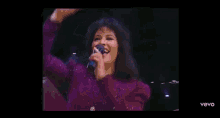a woman in a purple dress is singing into a microphone while smiling .