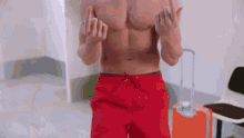 a shirtless man in red swim trunks is giving the middle finger