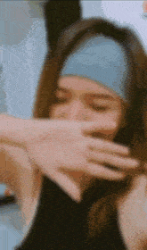 a woman wearing a blue headband is covering her mouth with her hand .