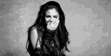 a black and white photo of a woman with long hair covering her mouth with her hand .
