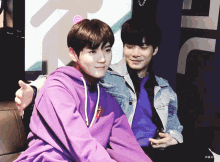 a man in a purple hoodie is sitting next to another man in a blue shirt